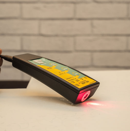 Handheld device with a red laser pointer on a light surface against a brick wall background