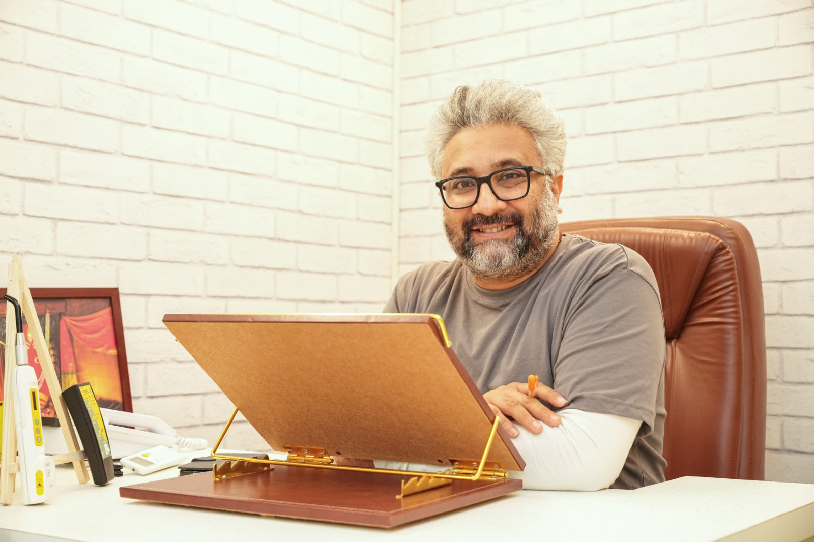 Man sitting at a desk with a tablet and stationery items, smiling.